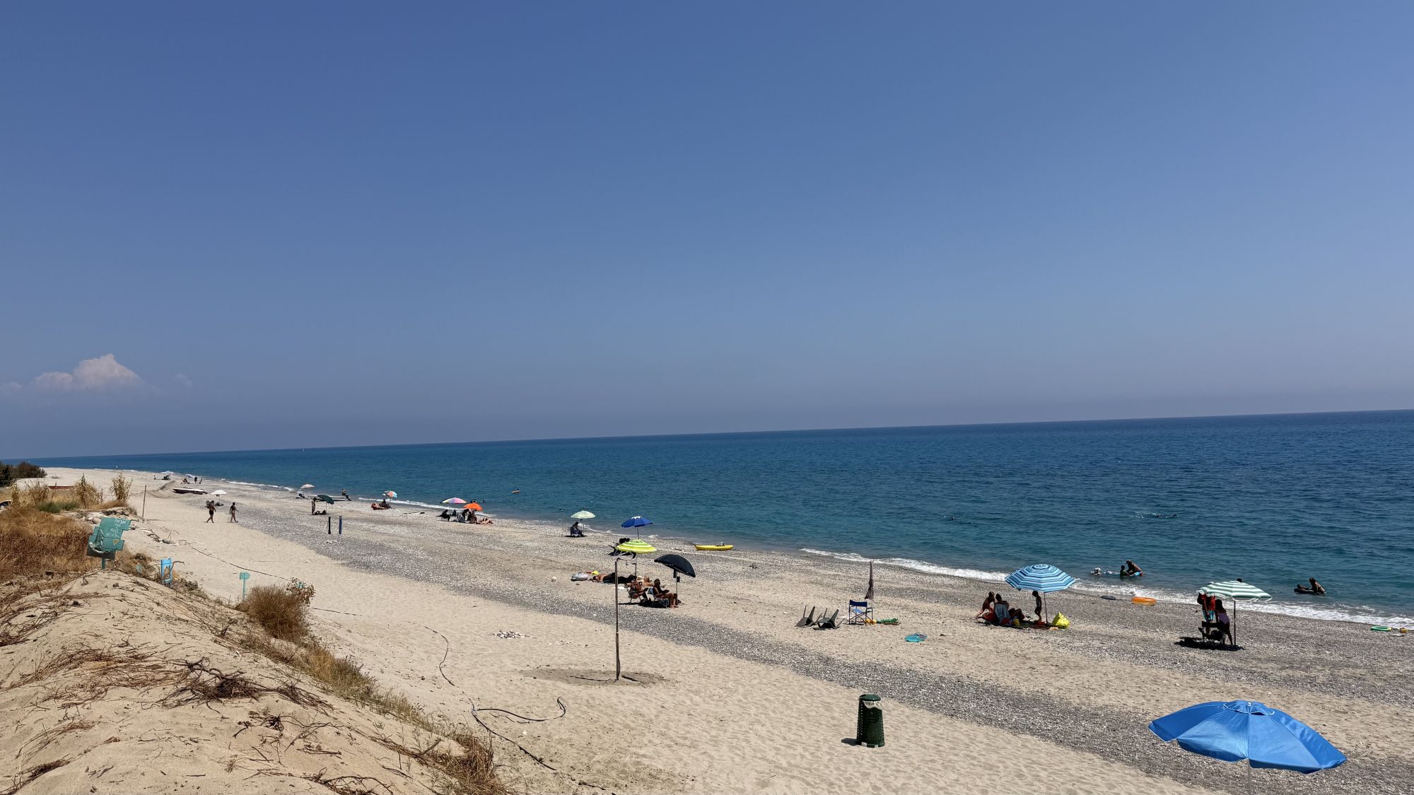 La spiaggia di Guardavalle Marina in estate: sabbia chiara, ombrelloni sparsi, dune e mare Ionio blu